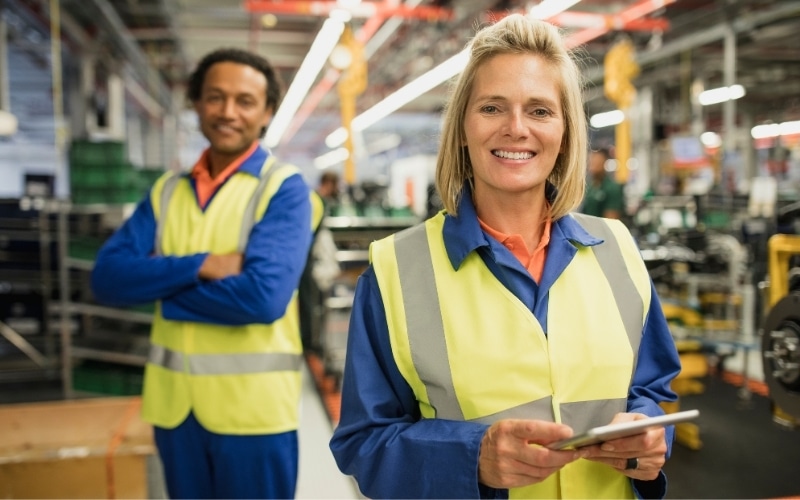 Two workers smile at the camera at a packaging facility.