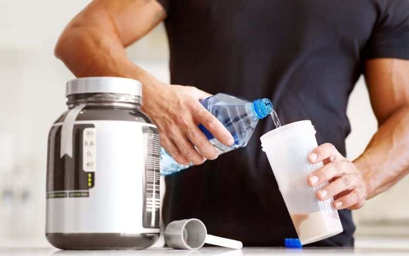 A man pours water into a cup to mix a protein drink.