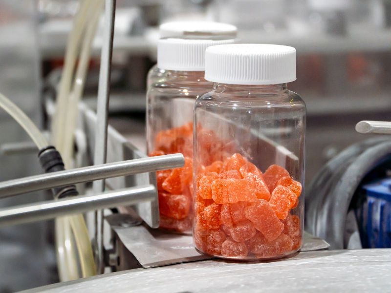 Orange gummy supplements are packaged in clear medicine bottles at a packaging facility.