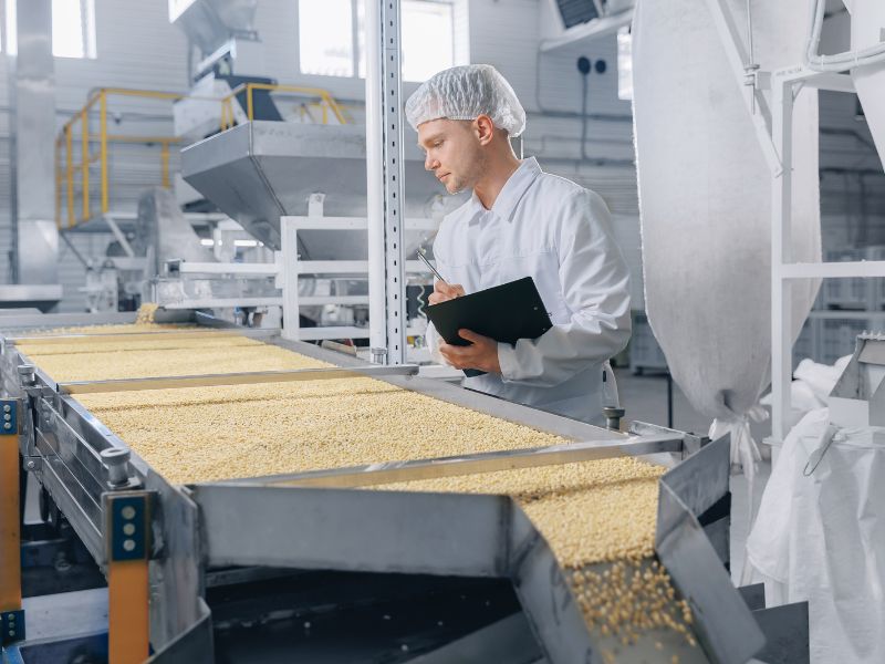 A food quality worker inspects food on a packaging production line, holding a tablet.
