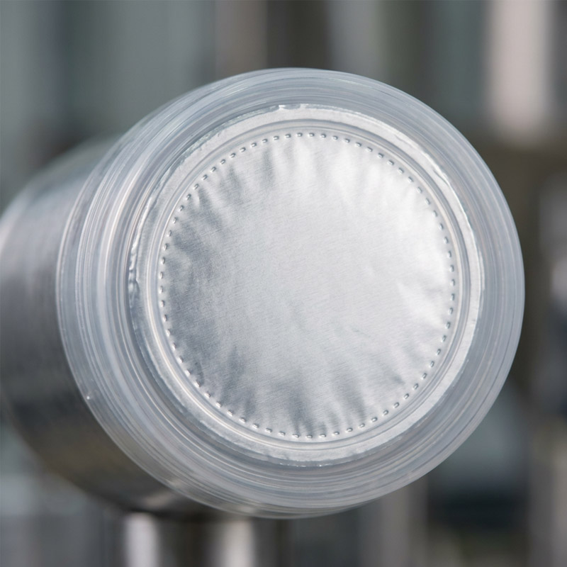 A close-up of a shiny, circular, metallic surface with a stitched border, encased in clear plastic, likely part of induction sealing equipment used for secure bottle sealing in industrial or scientific applications.