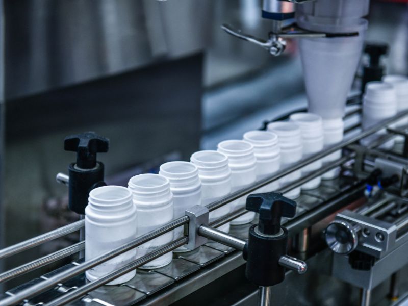 A line of white, plastic pill bottles move through a packaging machine.