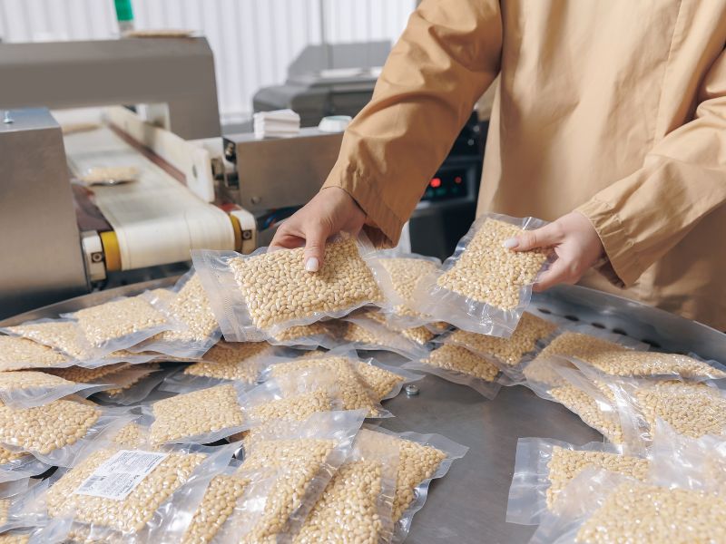 A person attempts to package their own food goods with a shrink-wrapping machine.