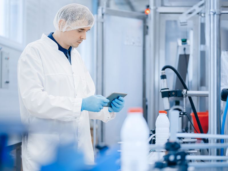 A food packaging worker looks at an iPad in front of a packaging machine.
