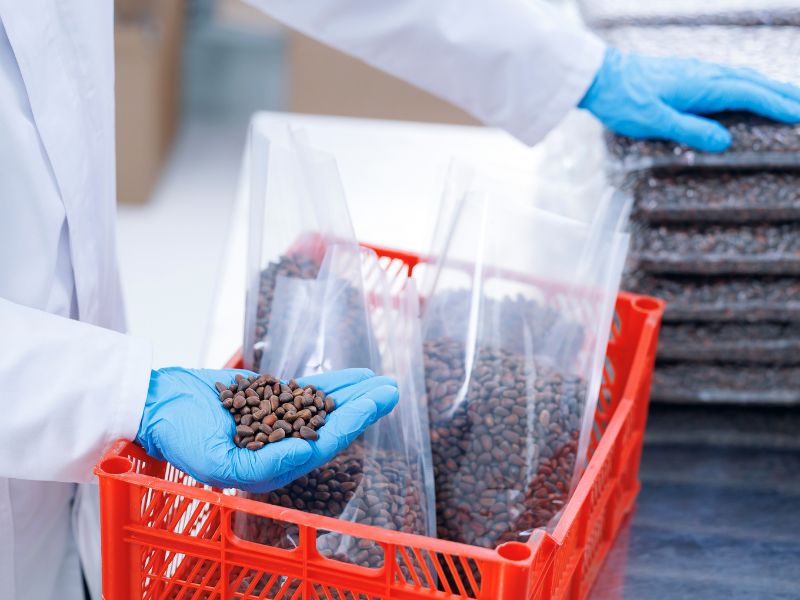 A food packaging worker wearing blue rubber gloves scoops coffee beans into his hand at a packaging facility.